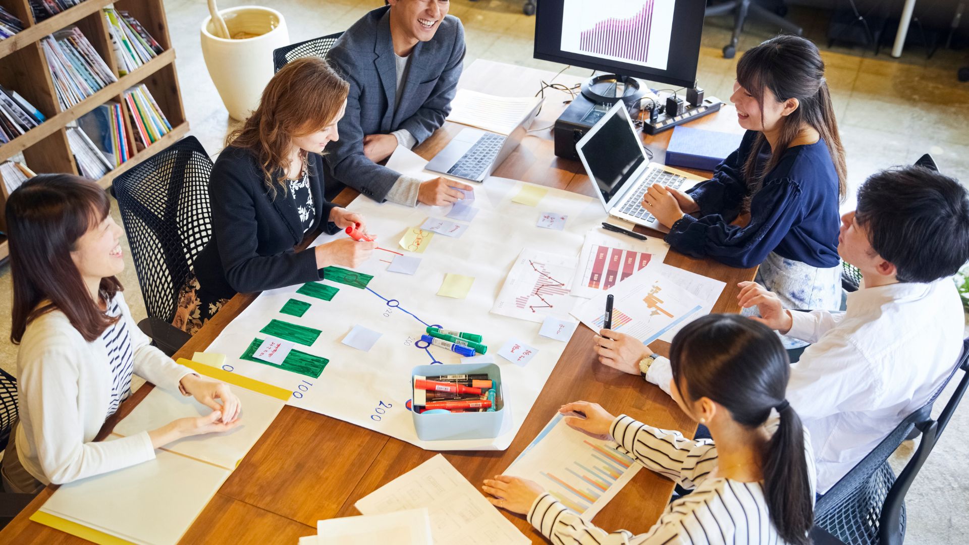 A cross-border team collaborating around a table with charts and sticky notes